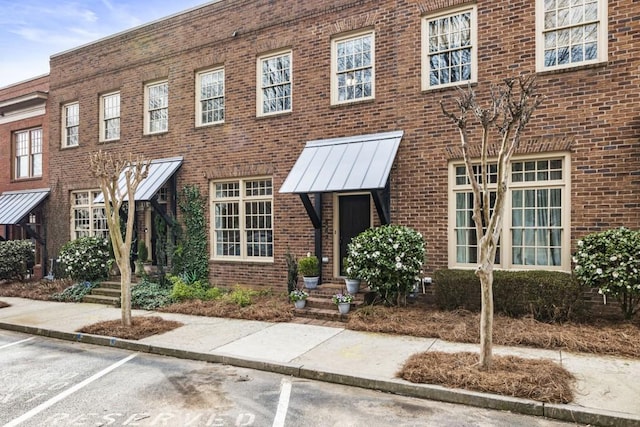 view of front of house with metal roof, brick siding, uncovered parking, and a standing seam roof