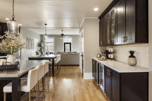 kitchen featuring backsplash, ceiling fan, dark brown cabinetry, open floor plan, and light wood-style flooring