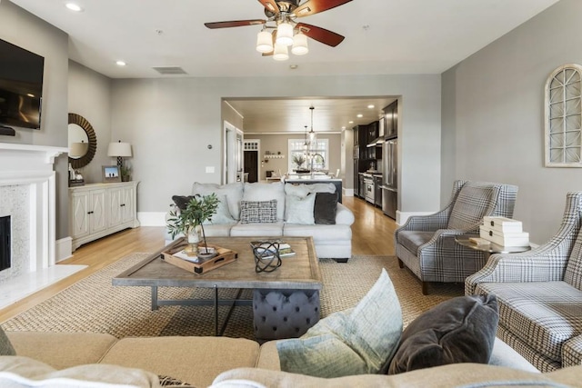 living room with light wood finished floors, visible vents, a fireplace, and a ceiling fan