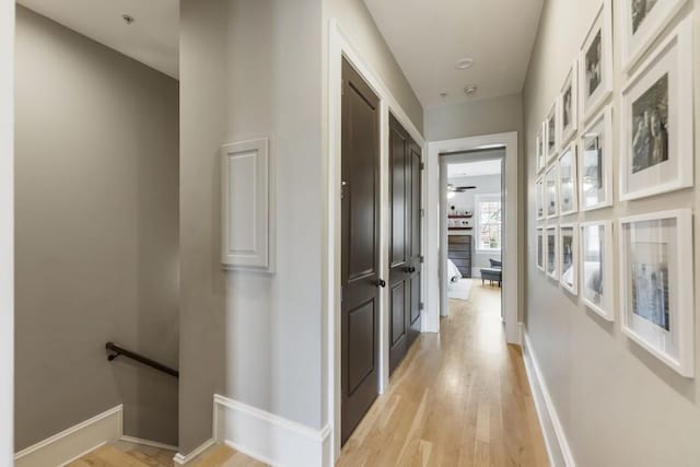 hallway with an upstairs landing, baseboards, and light wood finished floors