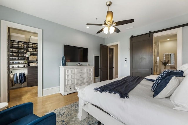 bedroom featuring light wood-style flooring, recessed lighting, a closet, a walk in closet, and a barn door