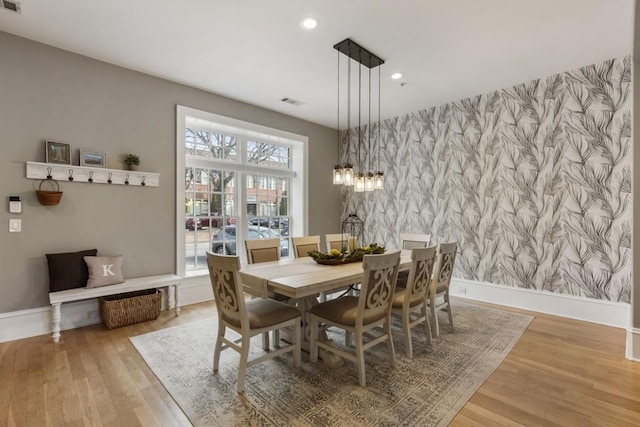 dining area with wallpapered walls, wood finished floors, baseboards, and an accent wall