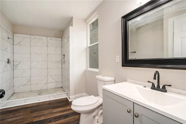 full bath featuring toilet, a tile shower, vanity, wood finished floors, and baseboards