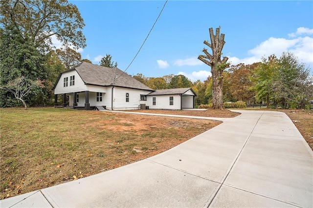 view of front facade featuring driveway, covered porch, a shingled roof, and a front yard