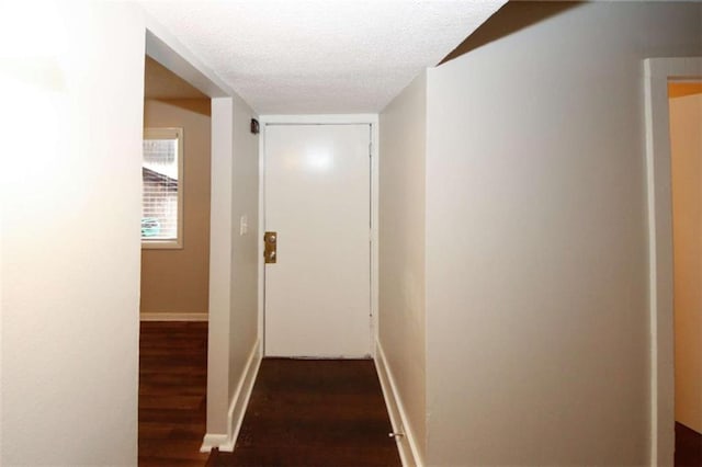 corridor with a textured ceiling and dark wood-type flooring