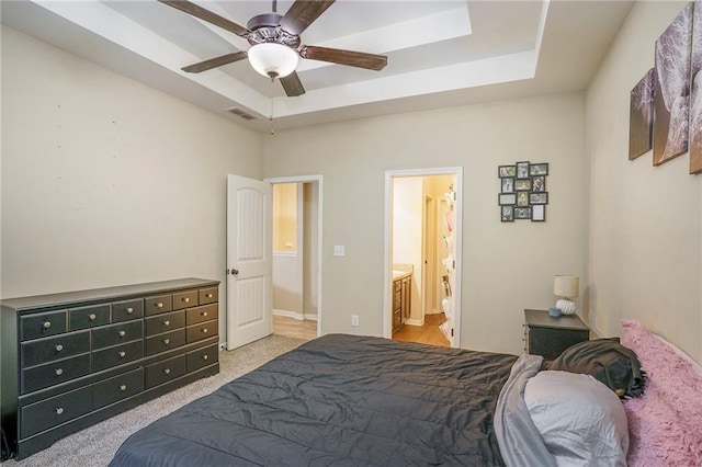 bedroom featuring light colored carpet, a raised ceiling, ceiling fan, and ensuite bath