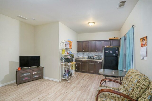 kitchen featuring tasteful backsplash, black fridge, dark brown cabinets, sink, and light hardwood / wood-style flooring