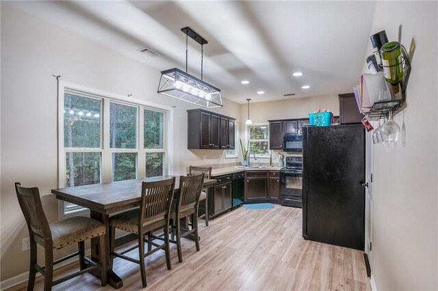 kitchen featuring sink, black appliances, pendant lighting, dark brown cabinets, and light wood-type flooring