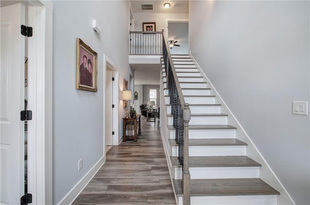 staircase featuring visible vents, baseboards, a high ceiling, and wood finished floors