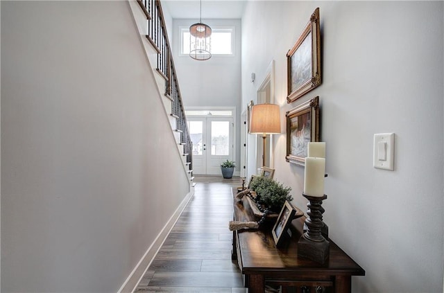 hallway featuring a notable chandelier, wood finished floors, stairway, baseboards, and a towering ceiling