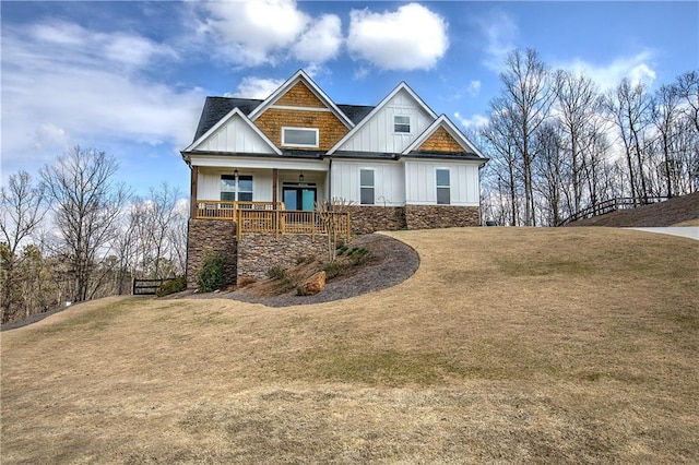 craftsman house featuring a porch, stone siding, board and batten siding, and a front yard