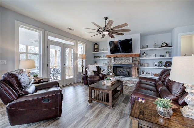 living area featuring visible vents, ceiling fan, french doors, a fireplace, and wood finished floors