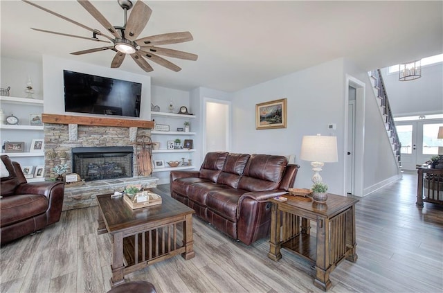 living area with ceiling fan, built in features, stairs, a fireplace, and wood finished floors