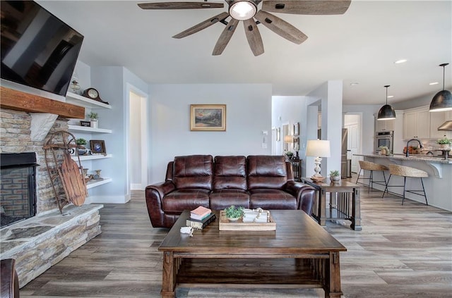 living room with recessed lighting, light wood-type flooring, a stone fireplace, and ceiling fan