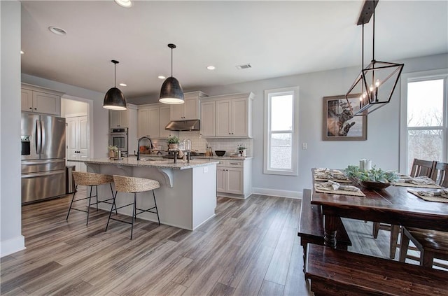 kitchen featuring visible vents, a breakfast bar, decorative backsplash, under cabinet range hood, and appliances with stainless steel finishes