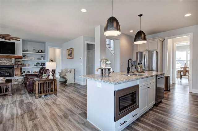 kitchen with light stone countertops, a fireplace, wood finished floors, stainless steel appliances, and a sink