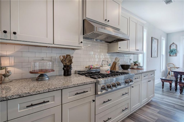 kitchen featuring light wood-style floors, tasteful backsplash, under cabinet range hood, and stainless steel gas cooktop