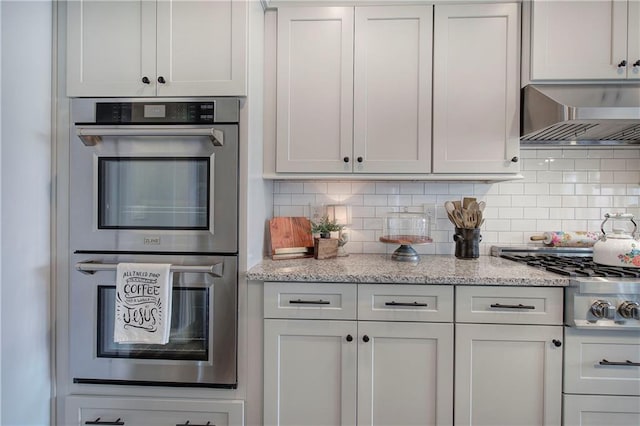 kitchen with stainless steel appliances, light stone countertops, backsplash, and wall chimney exhaust hood