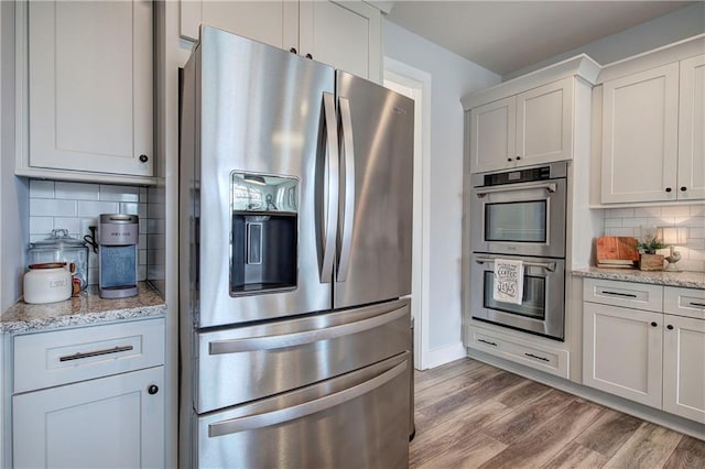 kitchen featuring light wood-type flooring, stainless steel appliances, light stone counters, and tasteful backsplash