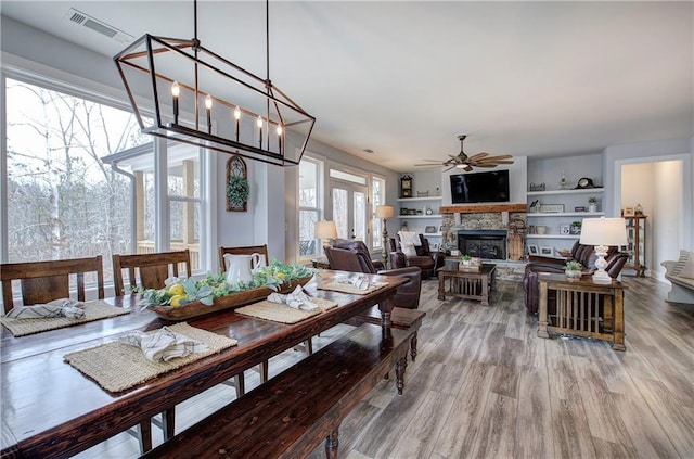 dining space featuring visible vents, a fireplace, wood finished floors, and a ceiling fan