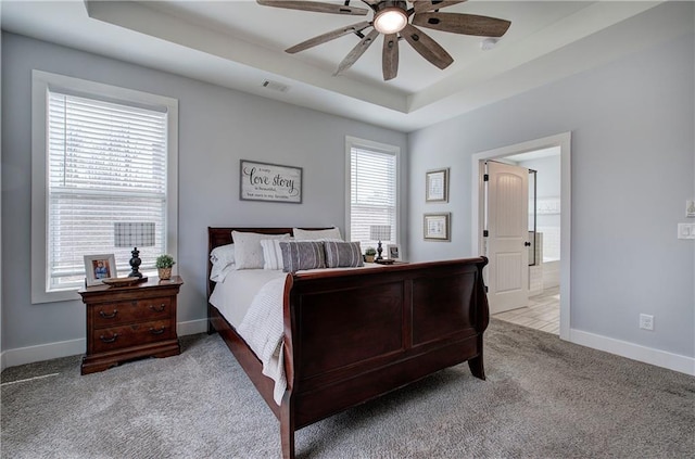 bedroom with a tray ceiling, multiple windows, baseboards, and carpet flooring