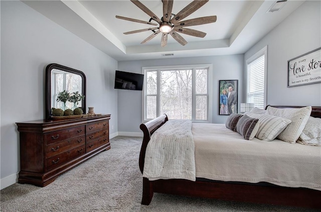 carpeted bedroom with baseboards, a tray ceiling, multiple windows, and visible vents