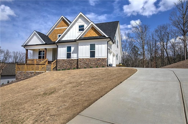 craftsman inspired home with stone siding, covered porch, board and batten siding, roof with shingles, and a garage