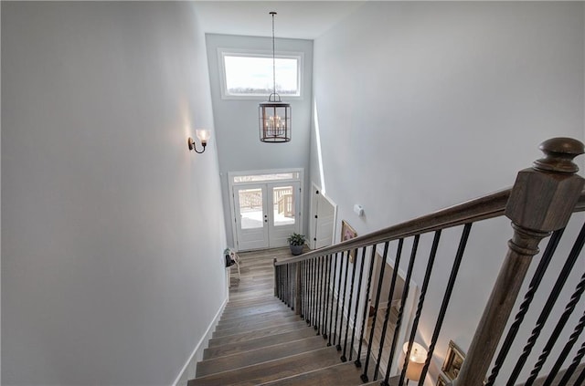 staircase with a high ceiling, a notable chandelier, wood finished floors, and baseboards