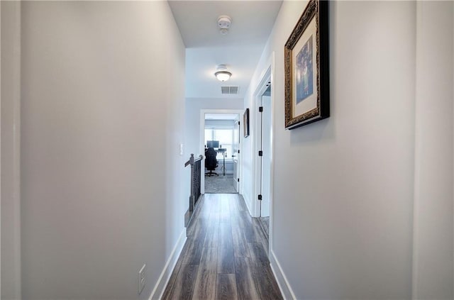 hallway with visible vents, baseboards, and dark wood-type flooring