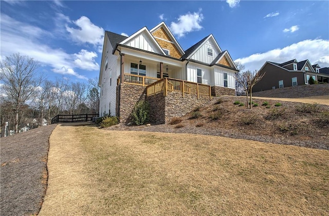 view of front of home with a front yard, covered porch, board and batten siding, and stone siding