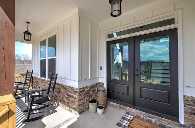 view of exterior entry with french doors, stone siding, board and batten siding, and covered porch