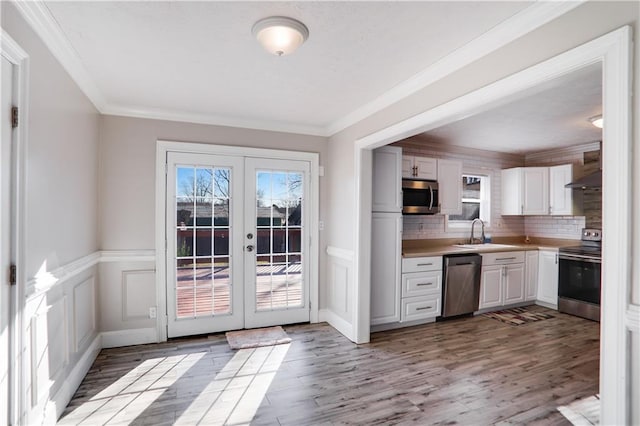 kitchen with stainless steel appliances, white cabinets, wall chimney exhaust hood, french doors, and backsplash