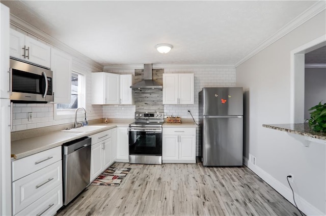 kitchen featuring stainless steel appliances, ornamental molding, white cabinets, wall chimney range hood, and sink