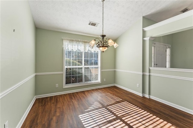 unfurnished dining area featuring decorative columns, dark wood-type flooring, a notable chandelier, and a textured ceiling