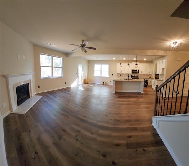 unfurnished living room with ceiling fan, a premium fireplace, dark hardwood / wood-style flooring, and sink