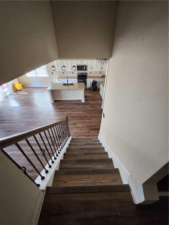 staircase featuring sink, wood-type flooring, and a high ceiling