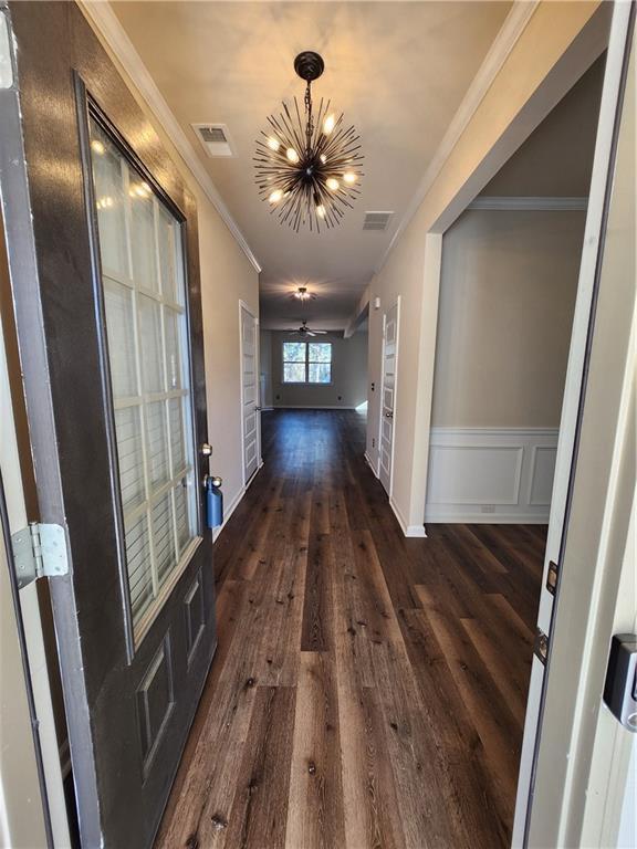 hallway with a notable chandelier, dark wood-type flooring, and ornamental molding