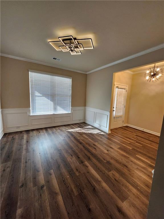 unfurnished living room featuring ornamental molding, an inviting chandelier, and dark hardwood / wood-style flooring