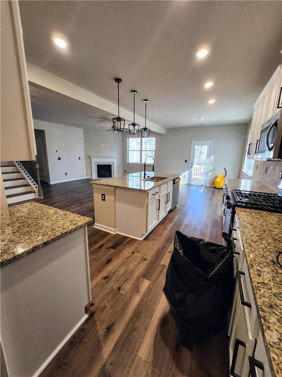 kitchen featuring sink, white cabinetry, stainless steel appliances, a center island with sink, and decorative light fixtures