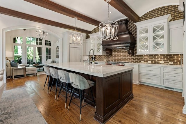 kitchen featuring sink, white cabinets, tasteful backsplash, hanging light fixtures, and a kitchen island with sink