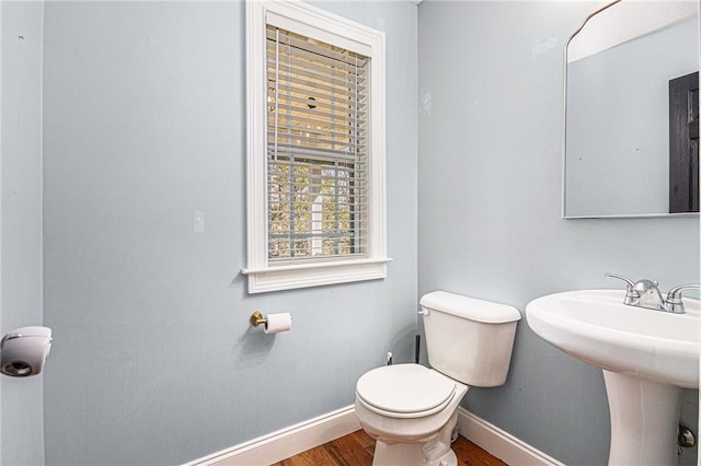bathroom with baseboards, toilet, wood finished floors, and a sink