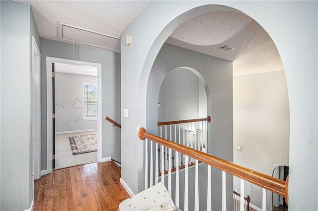corridor featuring an upstairs landing, attic access, a textured ceiling, wood-type flooring, and baseboards