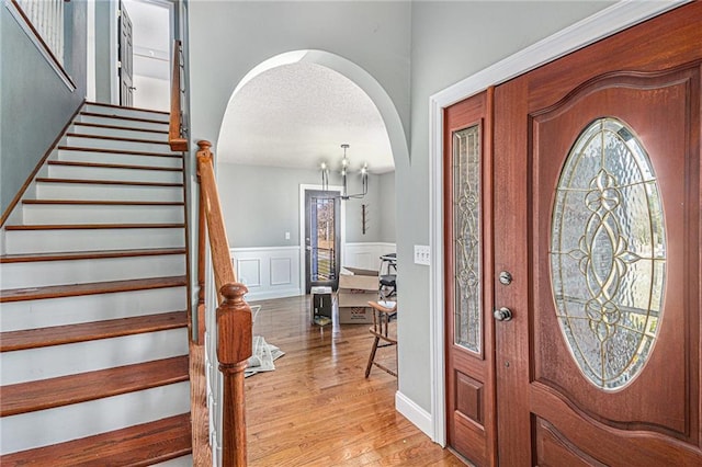entryway with stairway, a textured ceiling, a wainscoted wall, arched walkways, and wood finished floors