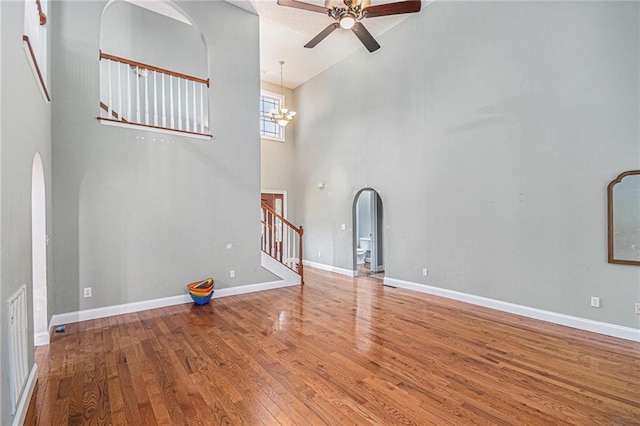 unfurnished living room featuring stairs, hardwood / wood-style flooring, arched walkways, and ceiling fan with notable chandelier