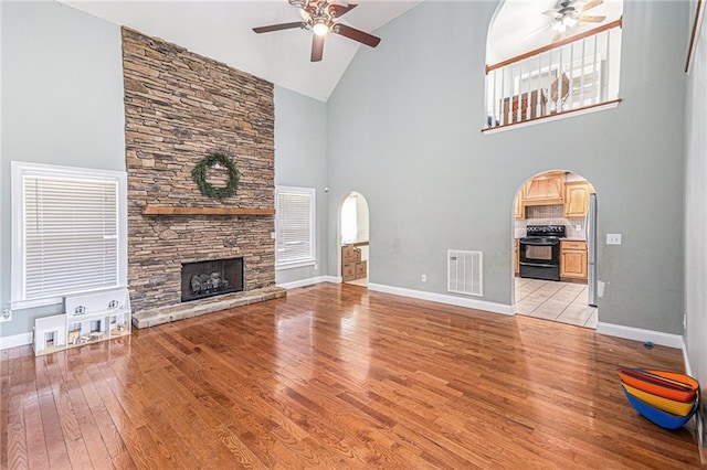 unfurnished living room featuring a ceiling fan, arched walkways, a stone fireplace, and light wood finished floors