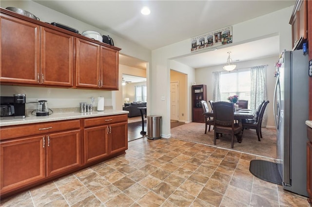 kitchen featuring brown cabinetry, freestanding refrigerator, light countertops, and baseboards