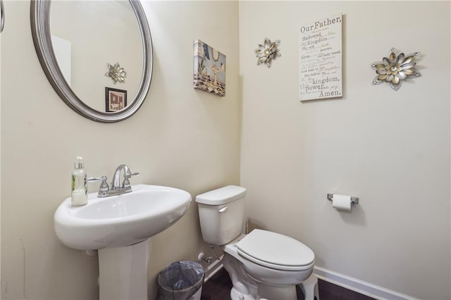 half bathroom featuring toilet, baseboards, and a sink