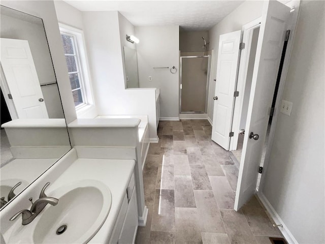 full bathroom with a stall shower, two vanities, baseboards, and a sink