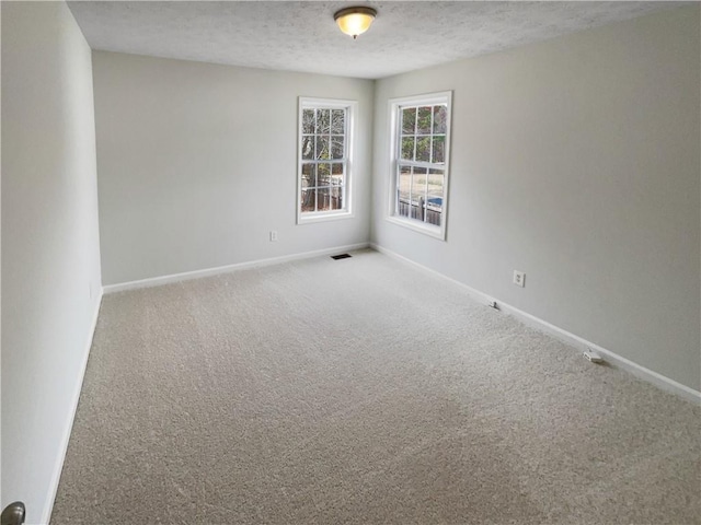 carpeted spare room with baseboards, visible vents, and a textured ceiling