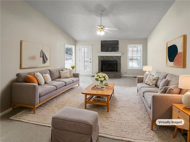 carpeted living area featuring a fireplace with raised hearth, baseboards, lofted ceiling, and a ceiling fan